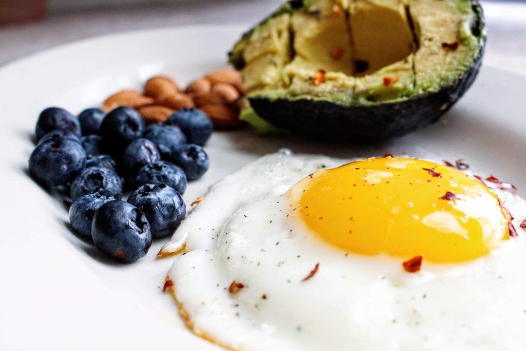 Teller mit Spiegelei, Avocado und Blaubeeren. Im Artikel: Wie viel Ei ist gesund?