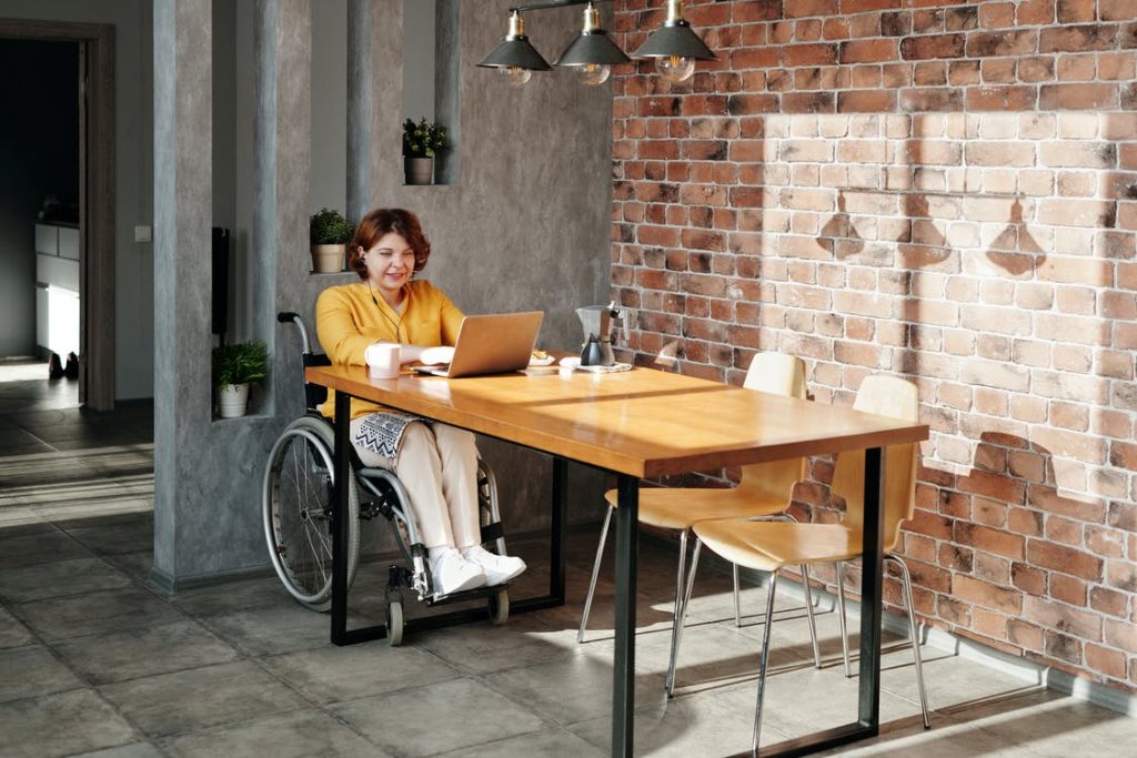 Frau im Rollstuhl sitzt am Schreibtisch. Im Artikel: Der Freistaat hilft Rollstuhlfahrern