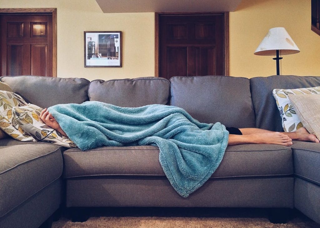 kranke Person auf Sofa mit Decke über Körper. Im Artikel: Ist schwitzen bei Fieber gesund?