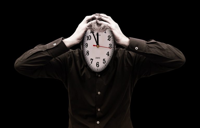 Ein Mann hat eine Uhr statt seines Kopfes auf den Schultern und hält diese Uhr so, als hätte er Kopfschmerzen.